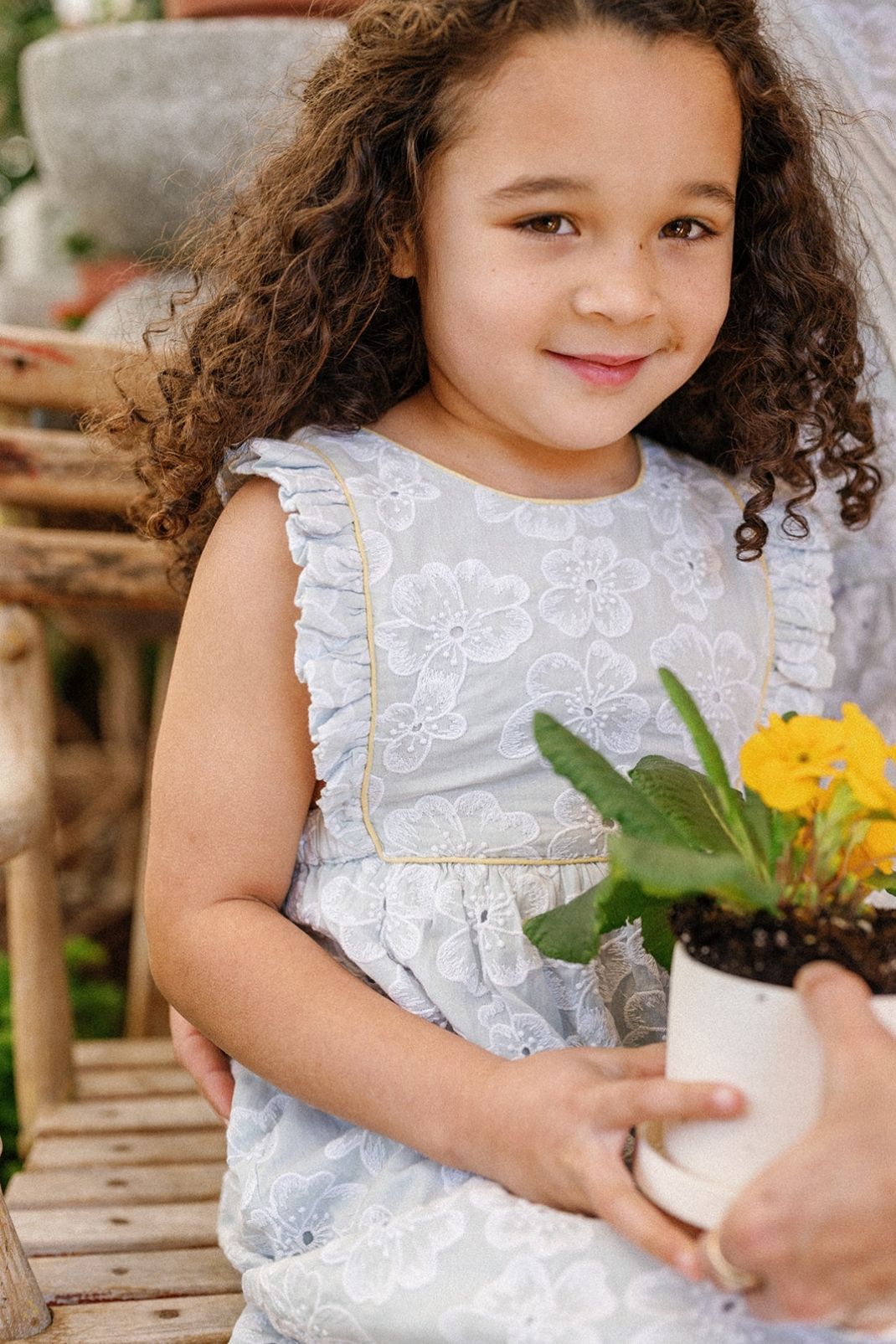 Little girl sitting holding a flower wearing the Elizabeth Dress in Sky Anemone Embroidery