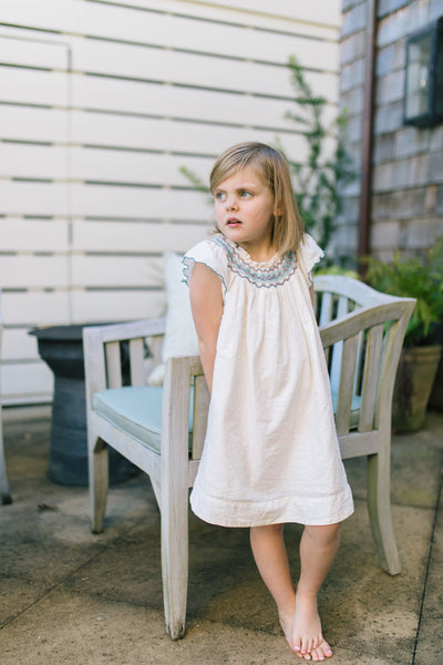 Little girl outside leaning against a chair wearing the Daisy Dress in Ivory