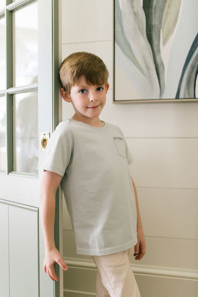 Little boy leaning against the door wearing the Henry T-Shirt in Pigeon with Thyme